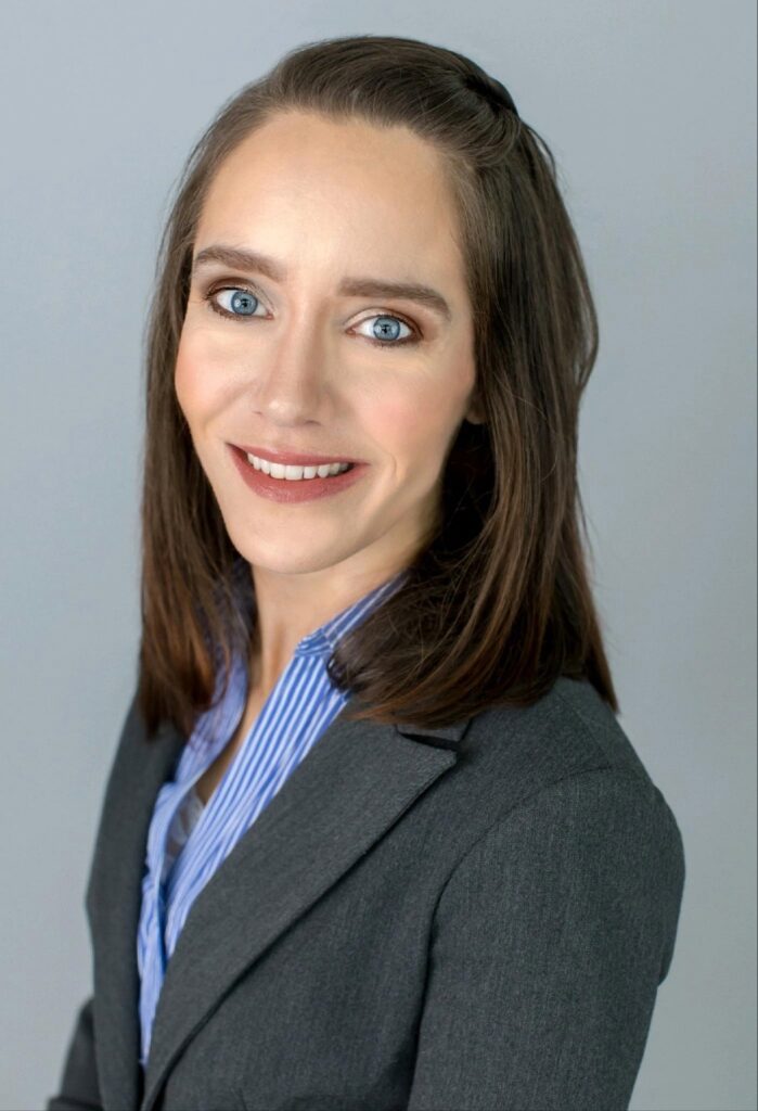 Headshot of Sarah Taylor in a grey blazer and blue striped shirt.